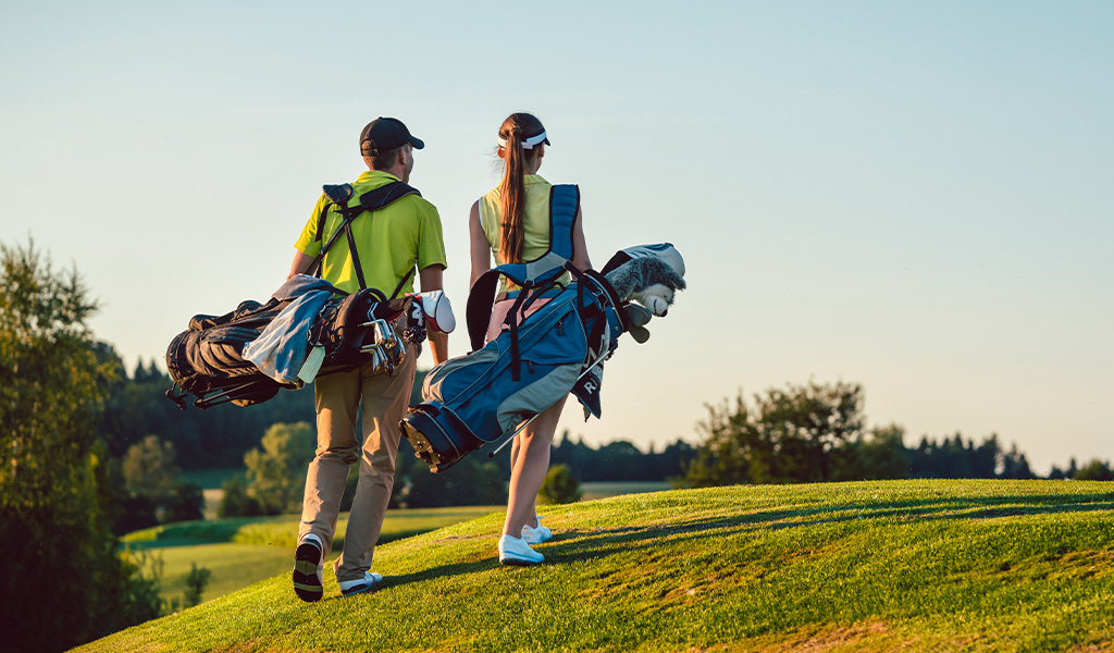 Man and Woman walking in a golf course with their golf bags